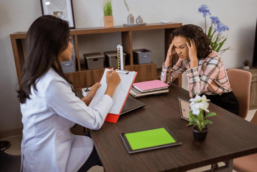 Female patient is depressed during a consultation with a doctor holding a tablet in the room